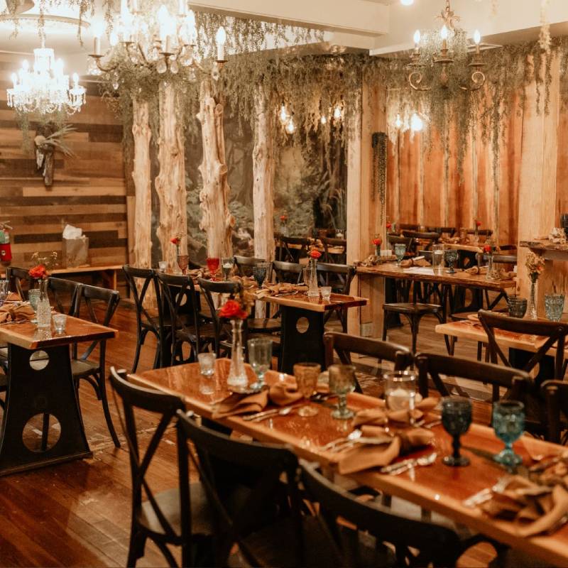 Live-edge wood tables and black cross-back chairs in the BoHo, under Spanish moss and Edison bulbs