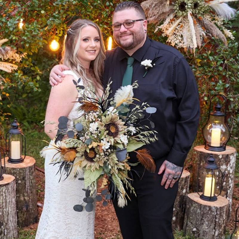 Bride and groom in front of the pampas and greenery arch outside the BoHo, lanterns set on log stumps