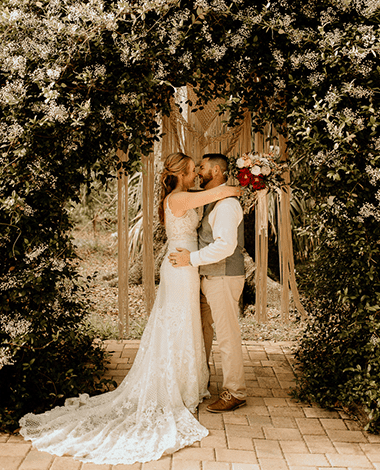 Bride and groom kissing under a jasmine-covered arch dressed with macramé