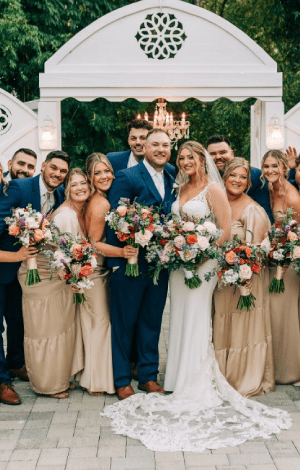 The wedding party under the white arbor, bridesmaids in champagne holding garden bouquets