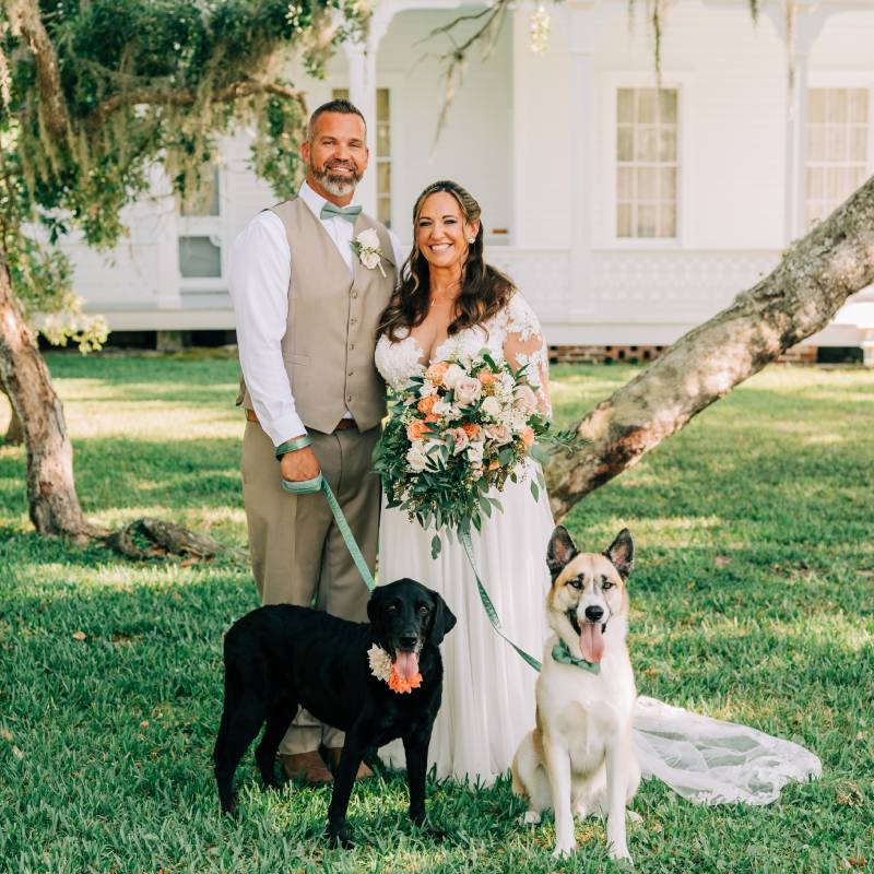 Couple and their two dogs on the lawn beneath a moss-draped oak, the manor house behind them